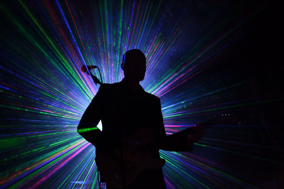 The silhouette of a man with a guitar in front of laser rays