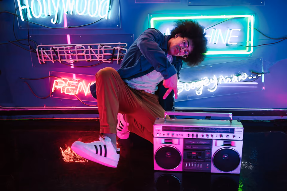 A man kneeling by a boombox in front of neon signs